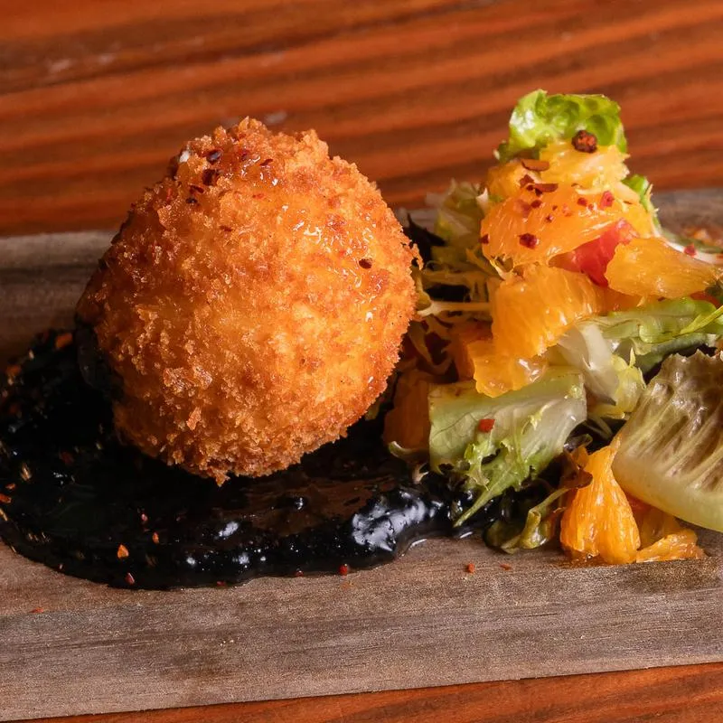 Golden fried ball, dark sauce, and orange salad on a wooden board.