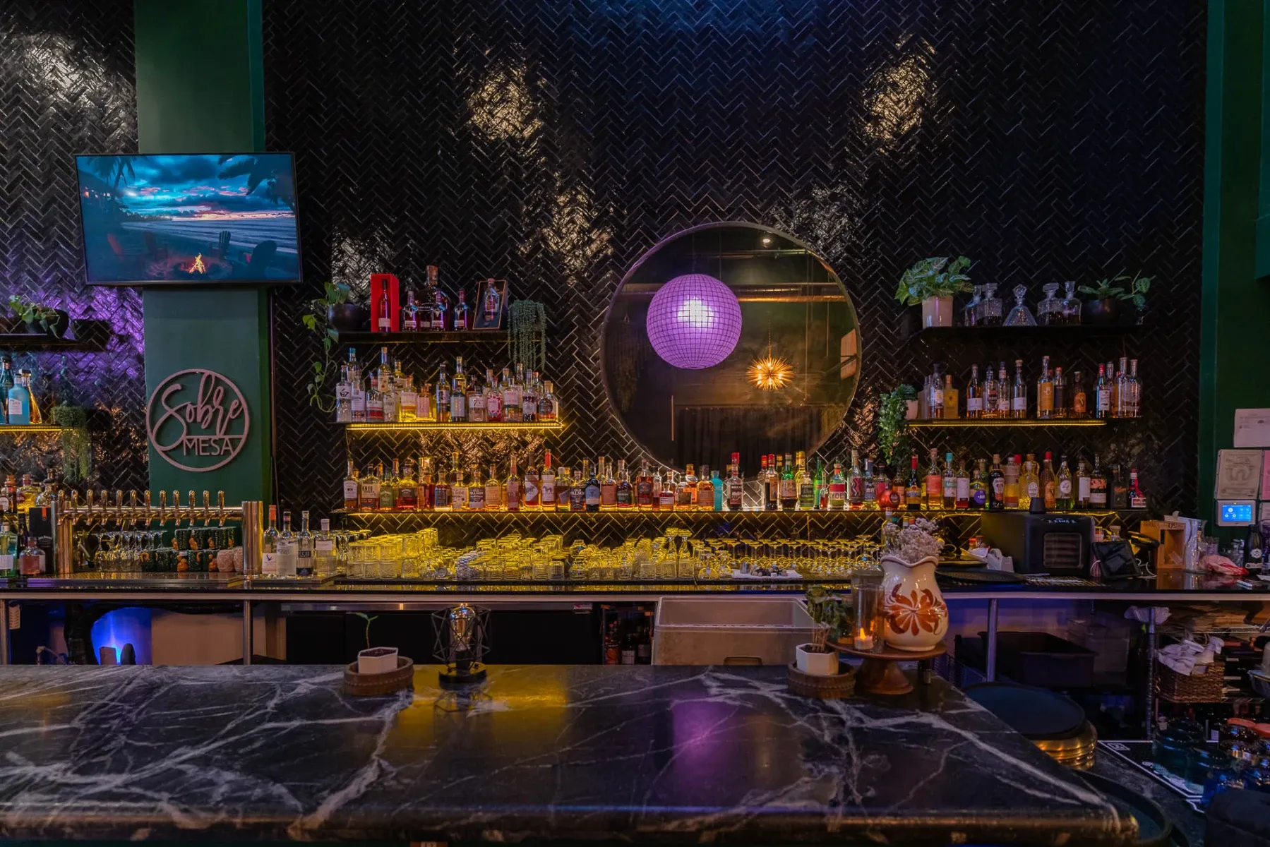 A long, well-stocked bar with a black marble countertop and disco ball.