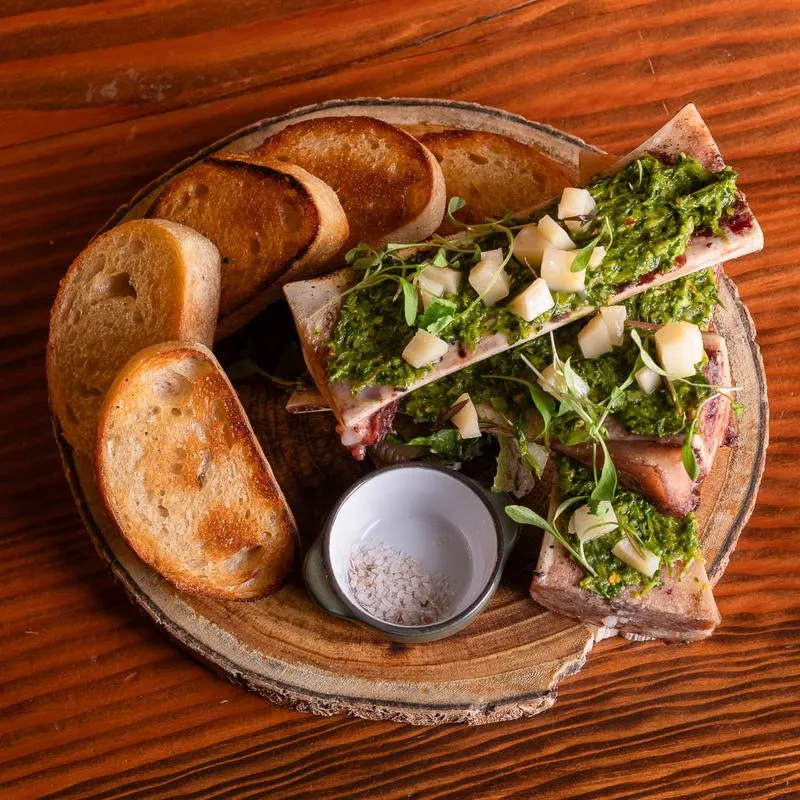 Bone marrow with green sauce, toast, and salt on wooden board.