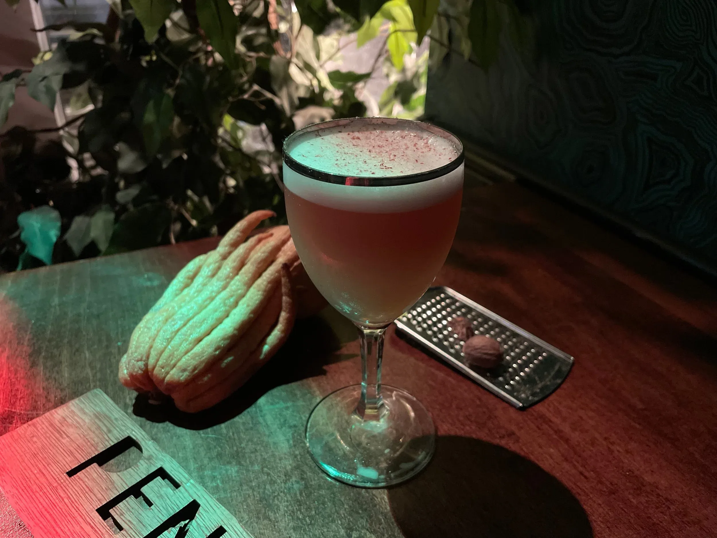 Foamy cocktail, Buddha's hand fruit, nutmeg, and grater on a table.