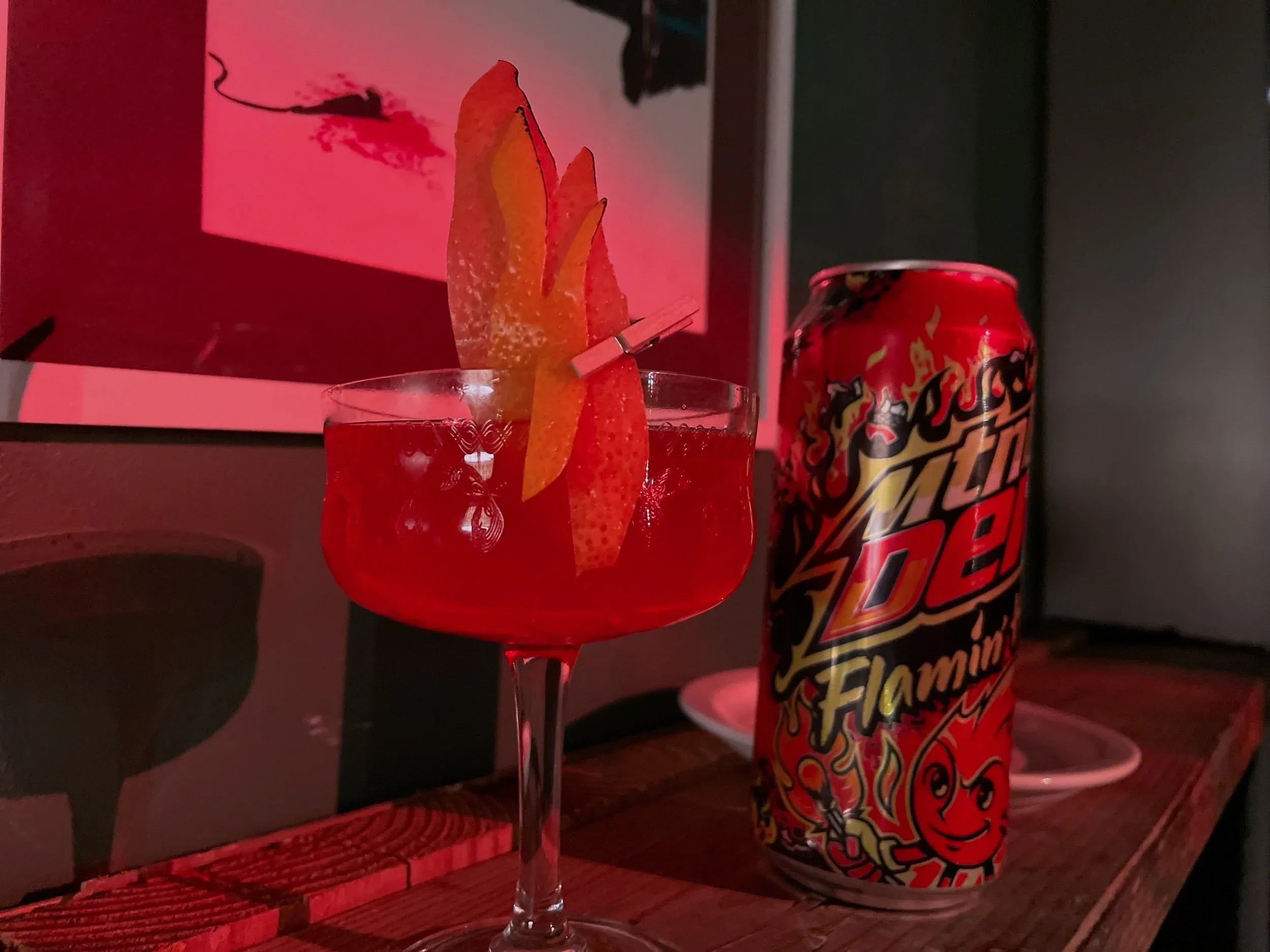 Red cocktail with orange peel garnish and a Mountain Dew Flamin' Hot can.