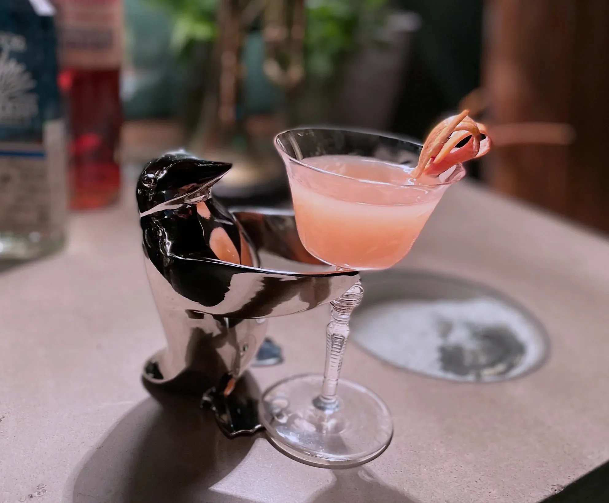 Penguin cocktail holder serving a pink drink with citrus garnish.