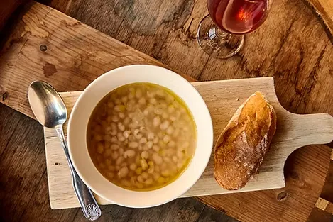 White bean soup, bread, spoon, and red wine on wooden table.