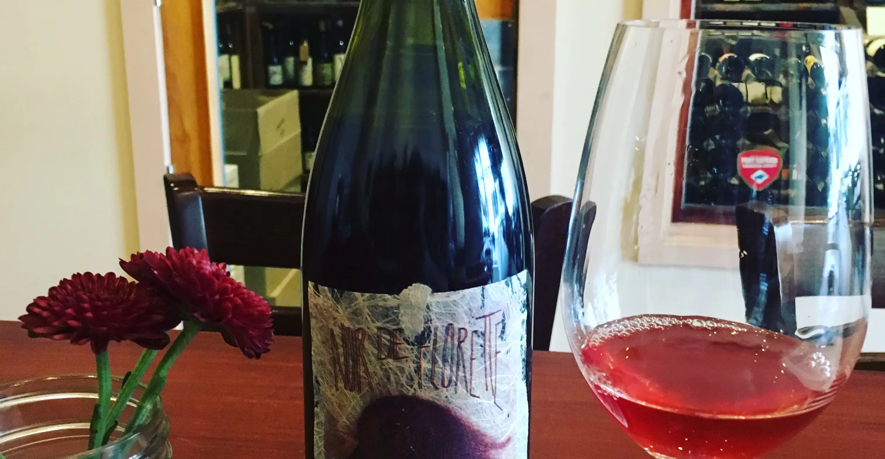 Green wine bottle, tilted glass of red wine, and red flowers.