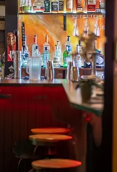 Bar counter with alcohol bottles, cocktail shakers, and red lighting.