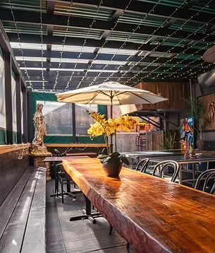 Outdoor patio with long wooden table, white umbrella, and yellow orchids.