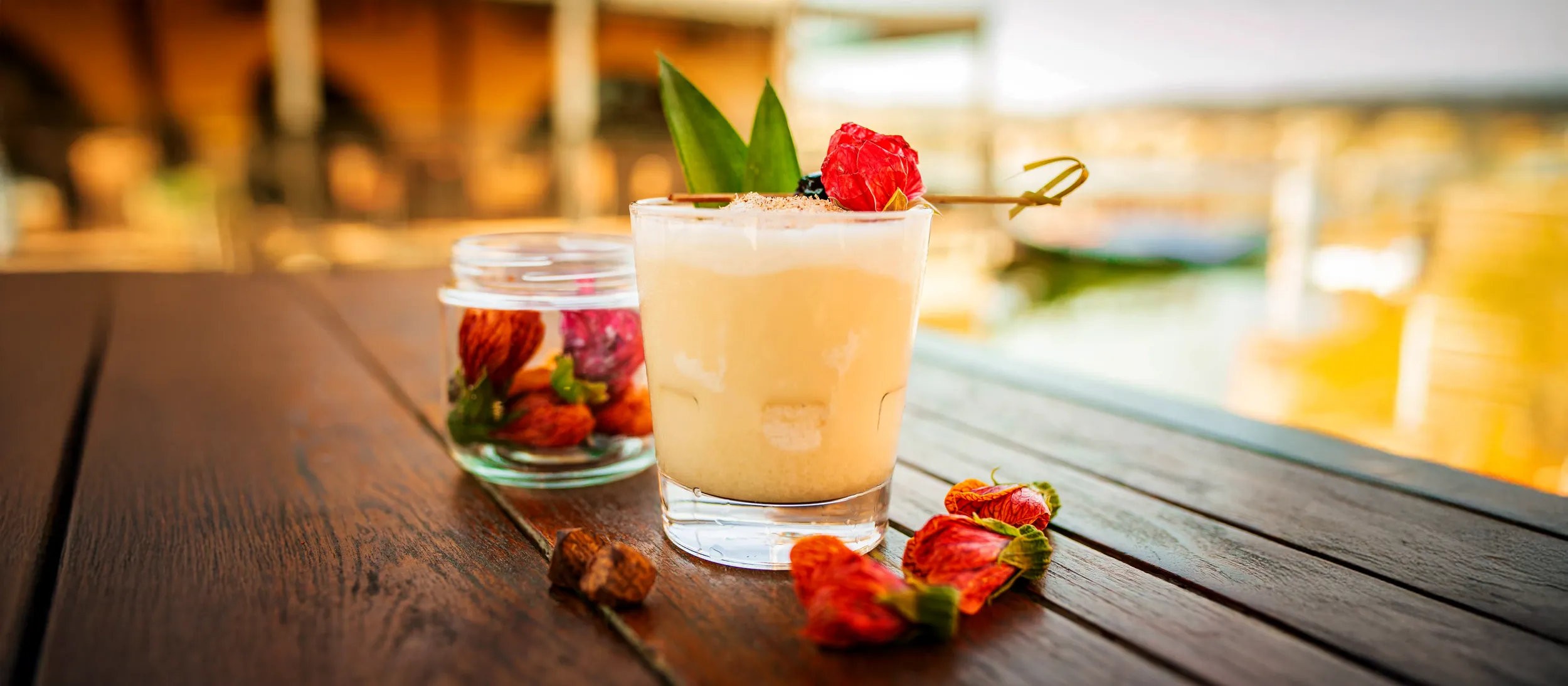 Creamy drink with red flower, green leaves, dried flowers on wooden table.