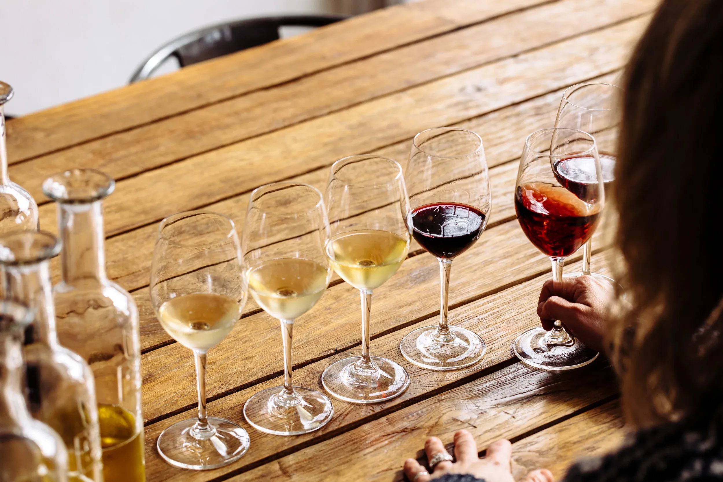 Hand holds red wine glass, white wine and bottles on wooden table.