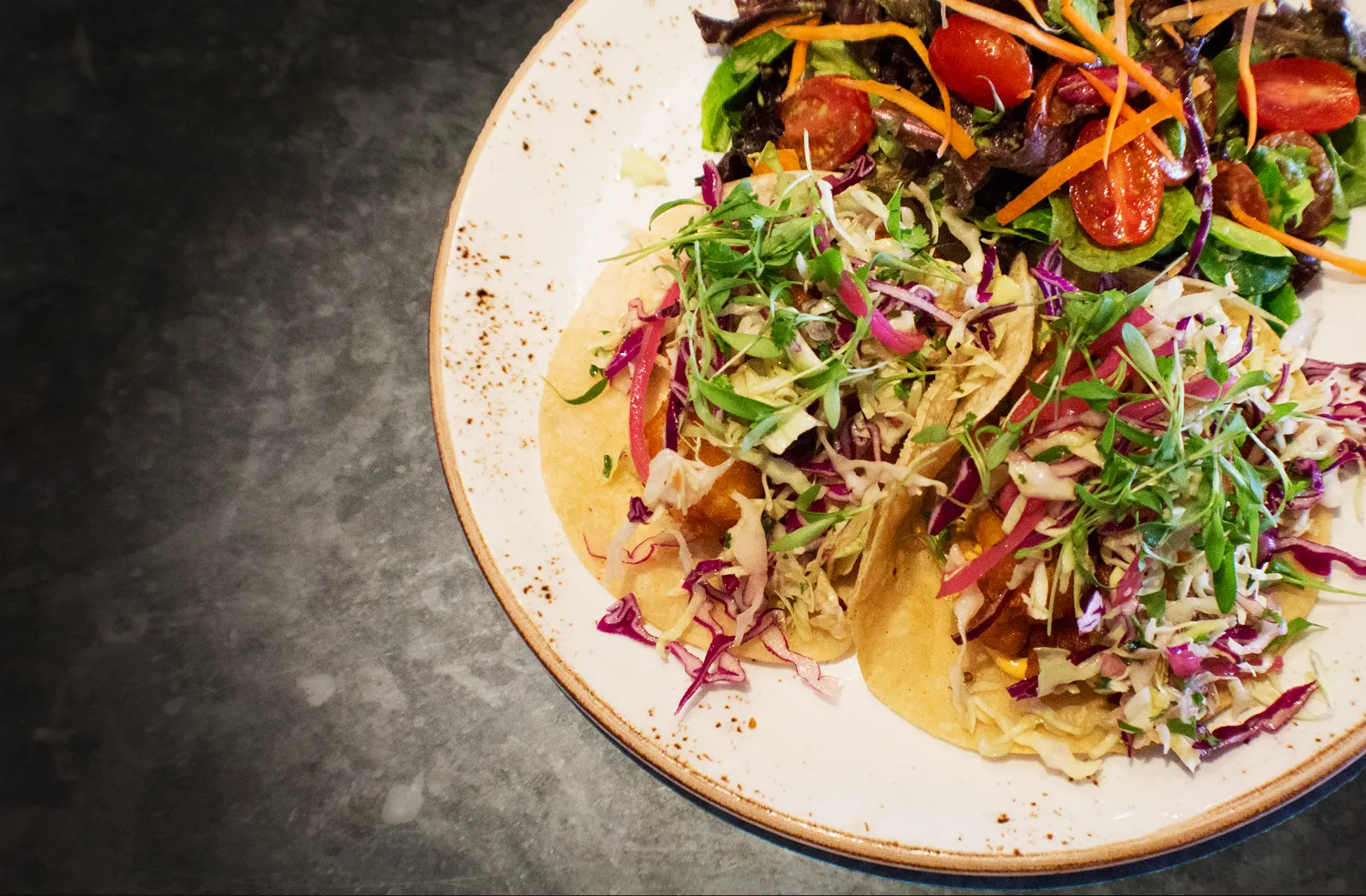 Tacos topped with purple and green cabbage, microgreens, and a side salad.