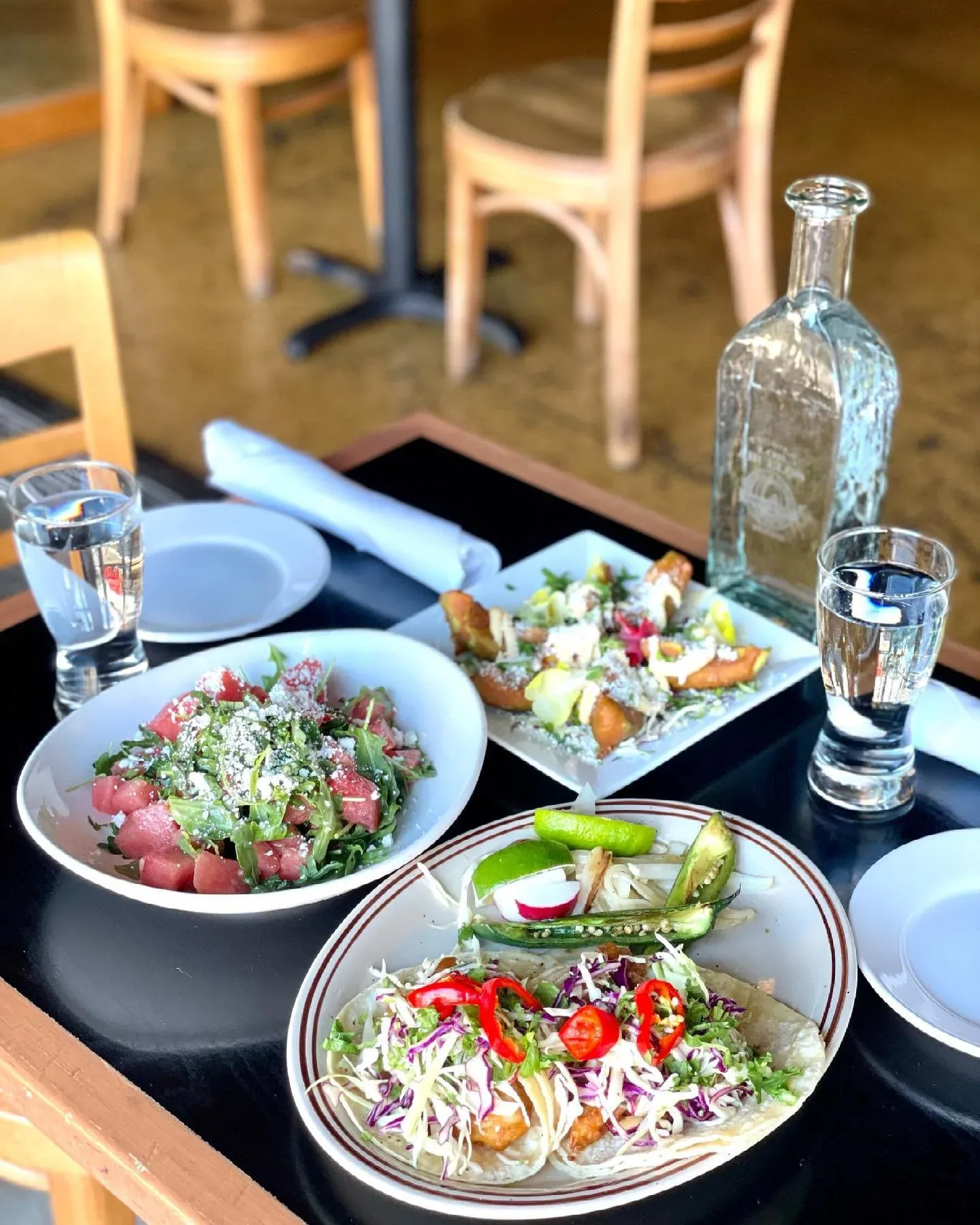 Restaurant table set with fish tacos, watermelon salad, and water.