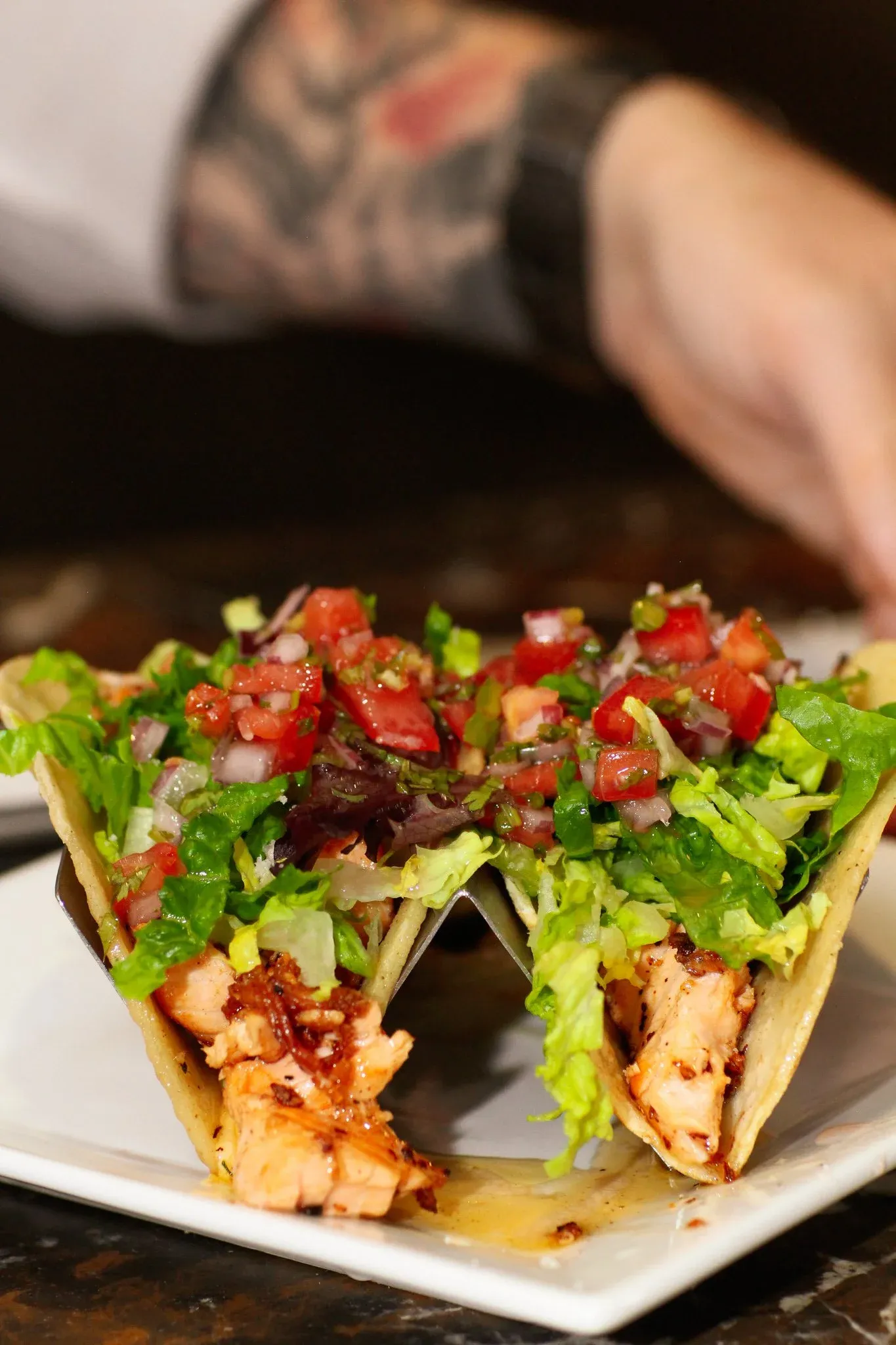 Two salmon tacos with lettuce, tomato, and onion on a plate.