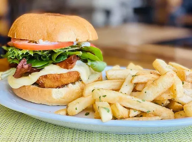 A burger with fried patty, bacon, cheese, lettuce, tomato, and fries.