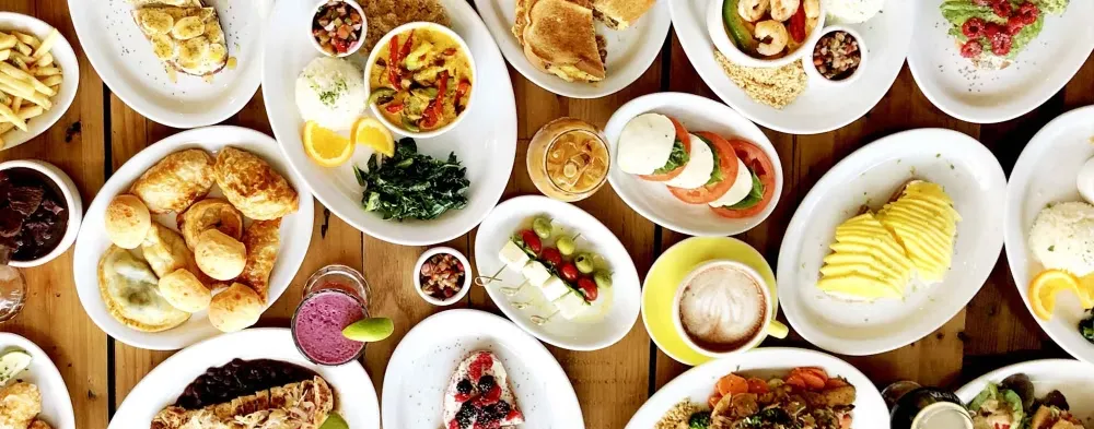 Numerous diverse dishes and beverages covering a wooden table, overhead view.