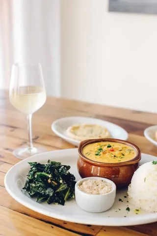 Plate of yellow stew, rice, greens, and white wine on a table.