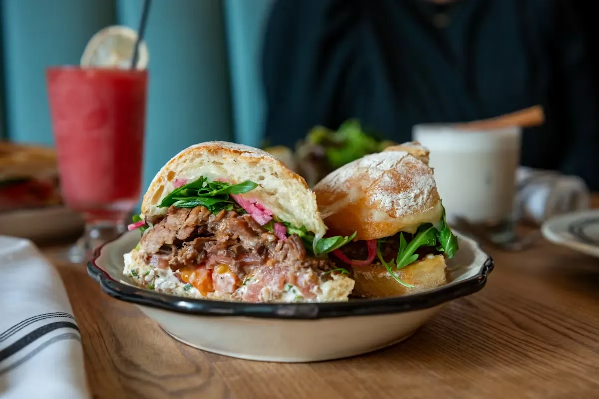 A pulled meat sandwich on a plate with drinks in the background.