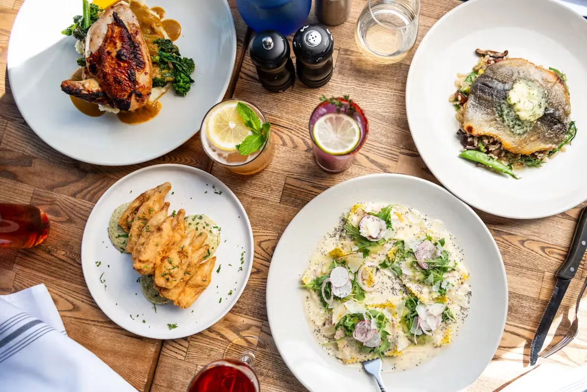 Table with roasted chicken, fish, pasta, fried food, and cocktails.