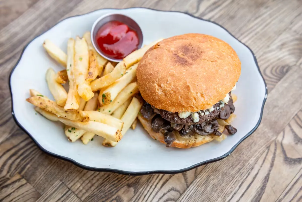 Burger with blue cheese, mushrooms, fries, and ketchup.