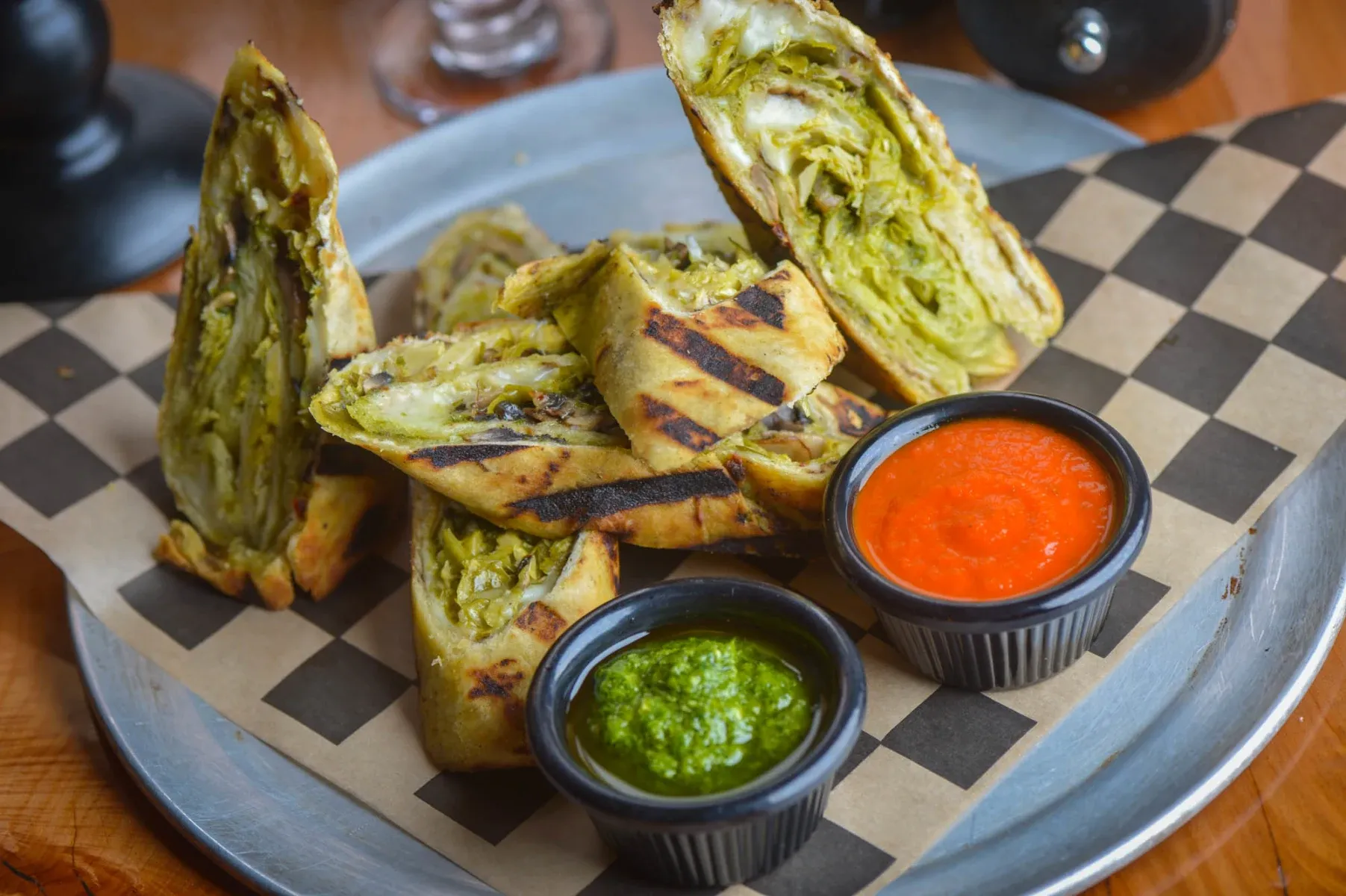 Grilled flatbread slices filled with greens, served with two dipping sauces.