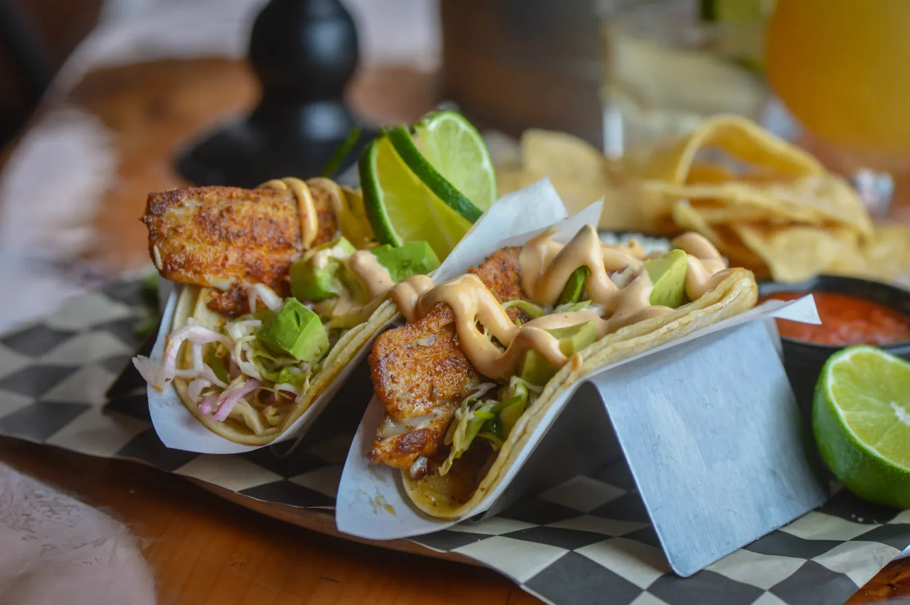 Two fish tacos with avocado, cabbage, sauce, and lime.