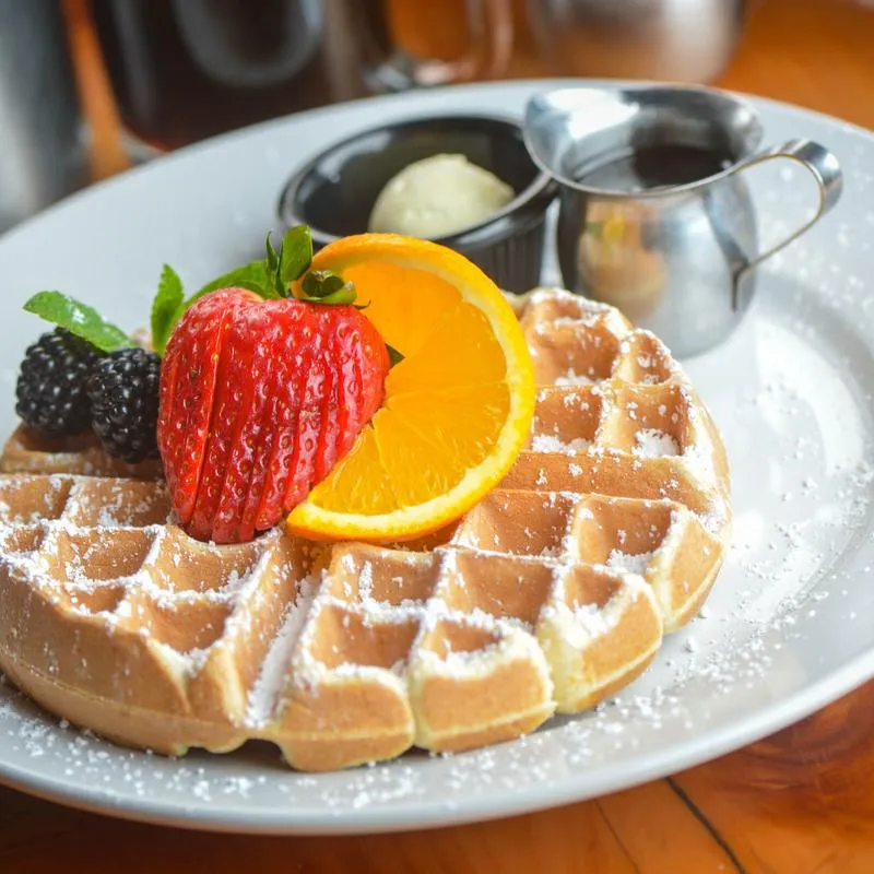 Waffle topped with strawberry, orange, blackberries, powdered sugar, butter, and syrup.