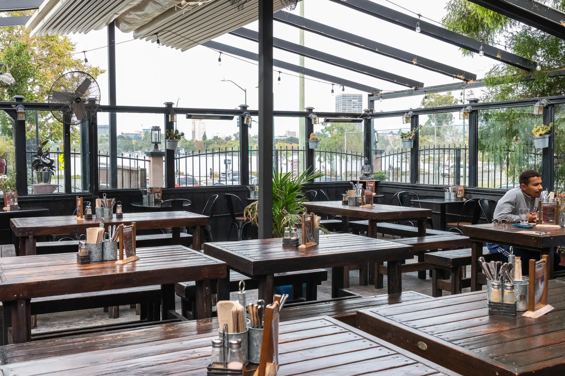 Covered outdoor restaurant with many dark wooden tables and one man.