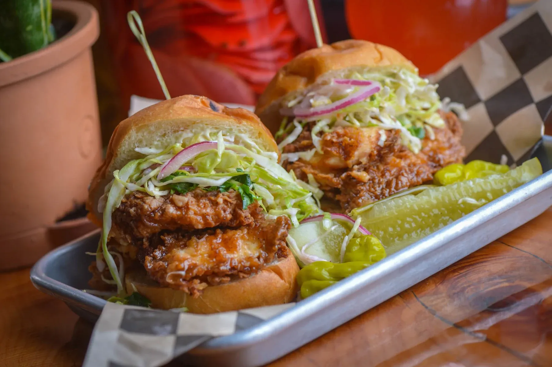 Two fried chicken sandwiches with coleslaw and pickles on a tray.
