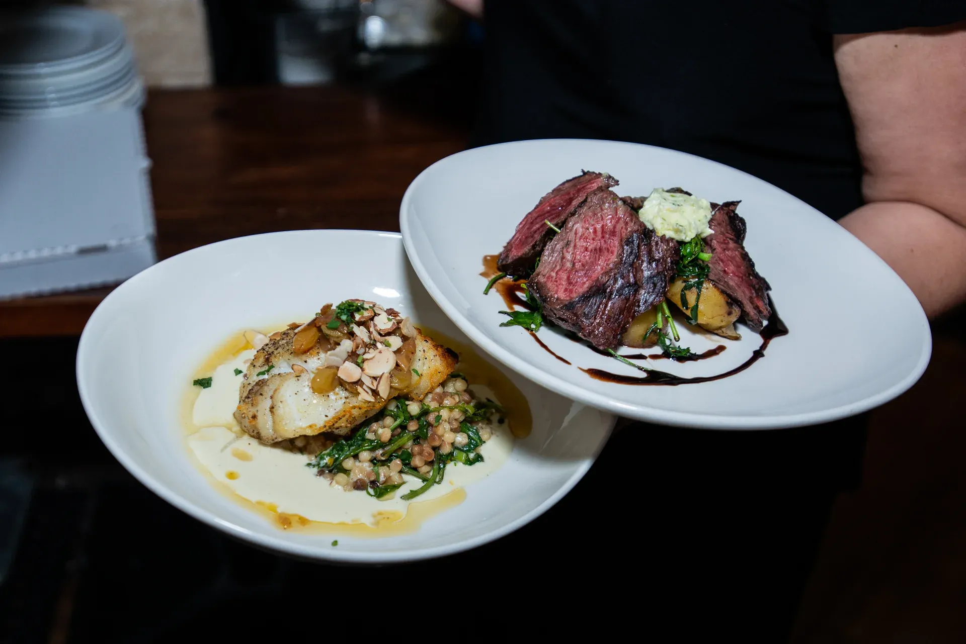 Two plates of plated food: fish with almonds and sliced steak.