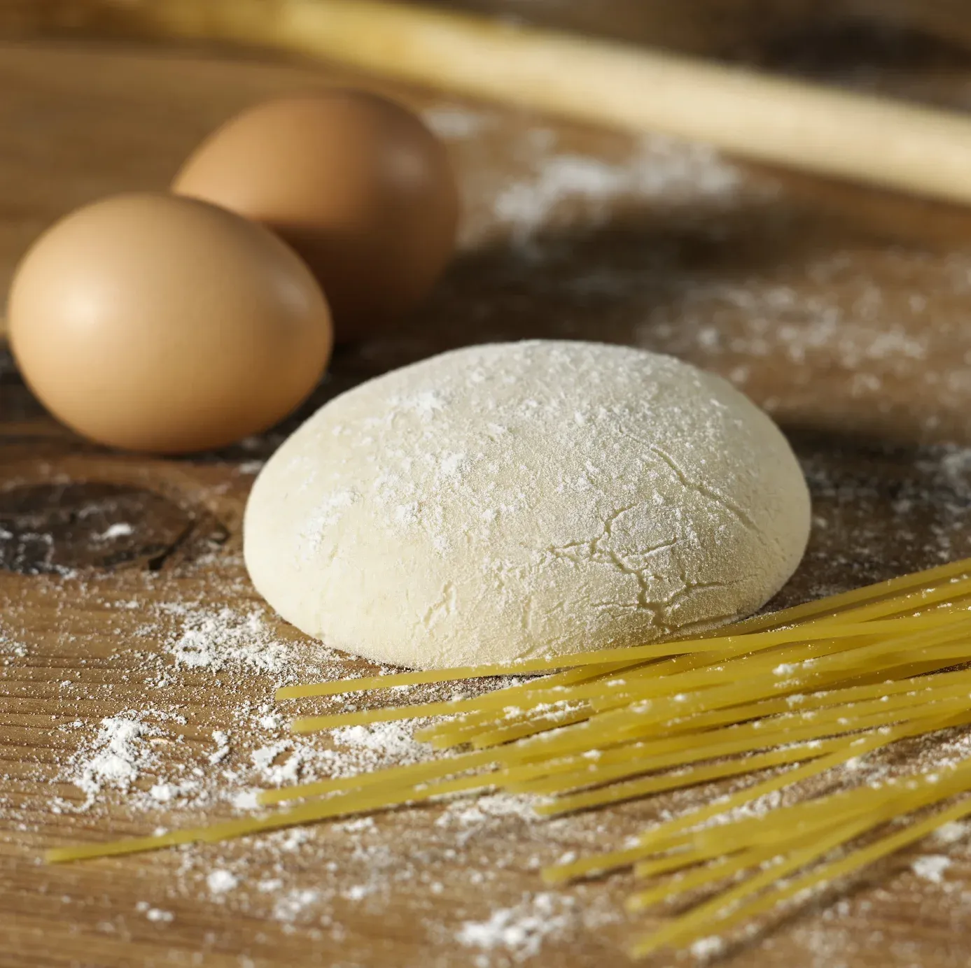 Two eggs, a dough ball, and spaghetti on a floured wooden surface.