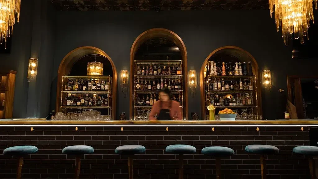An empty bar with a bartender behind an array of liquor bottles.