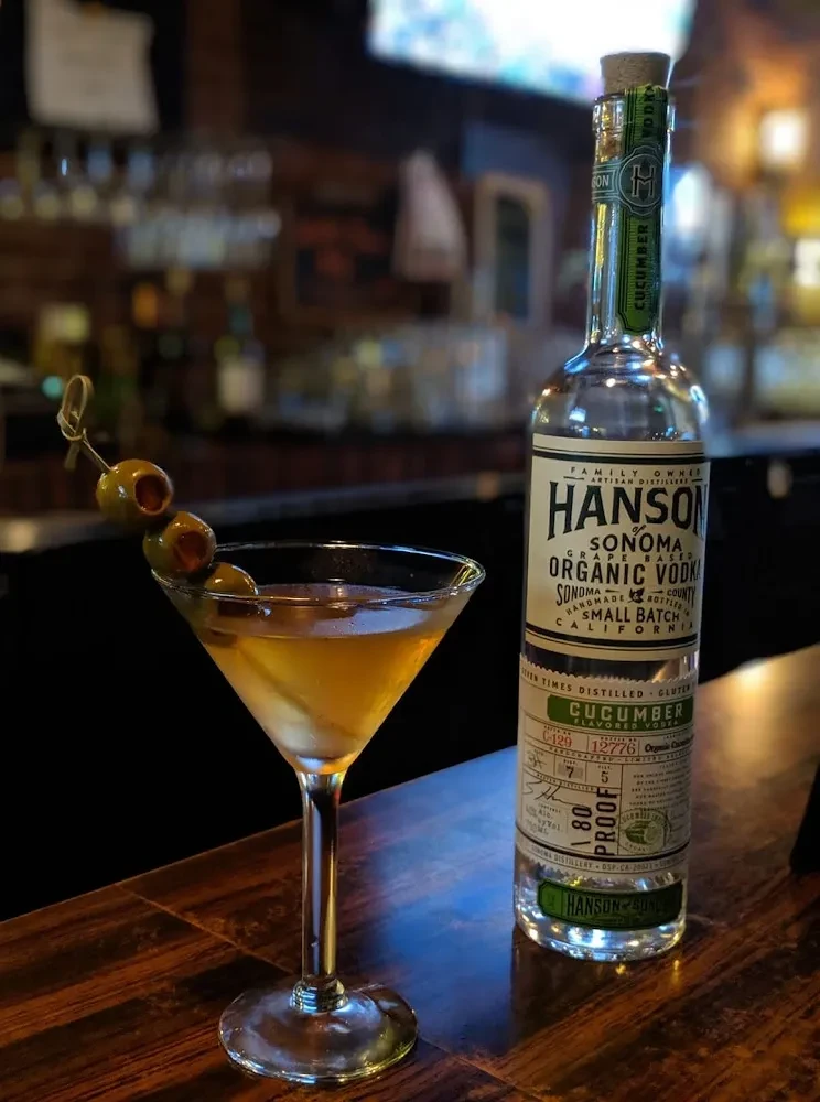 Martini with olives next to a bottle of Hanson Organic Cucumber Vodka.