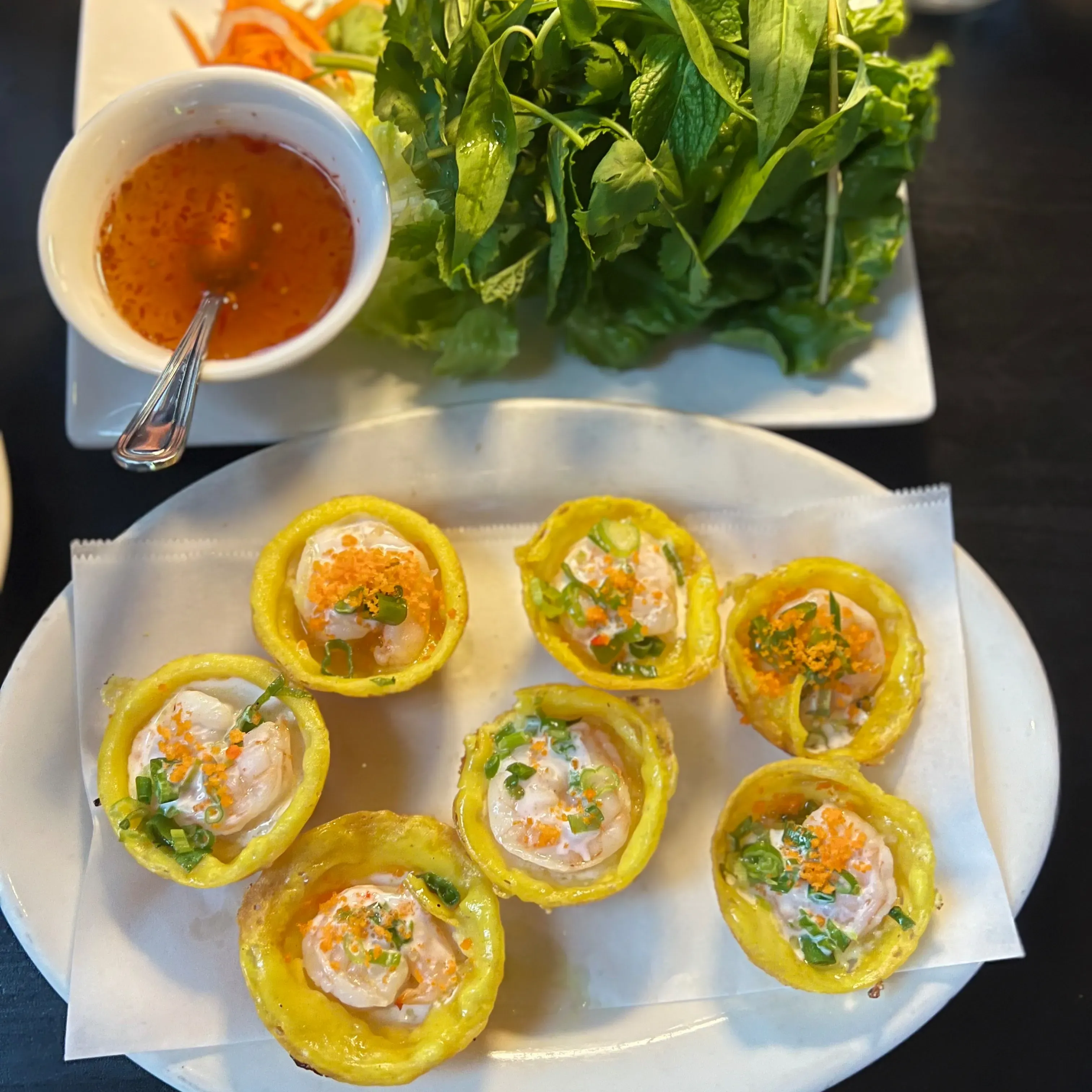 Crispy yellow shrimp cakes with a dipping sauce and green herbs.