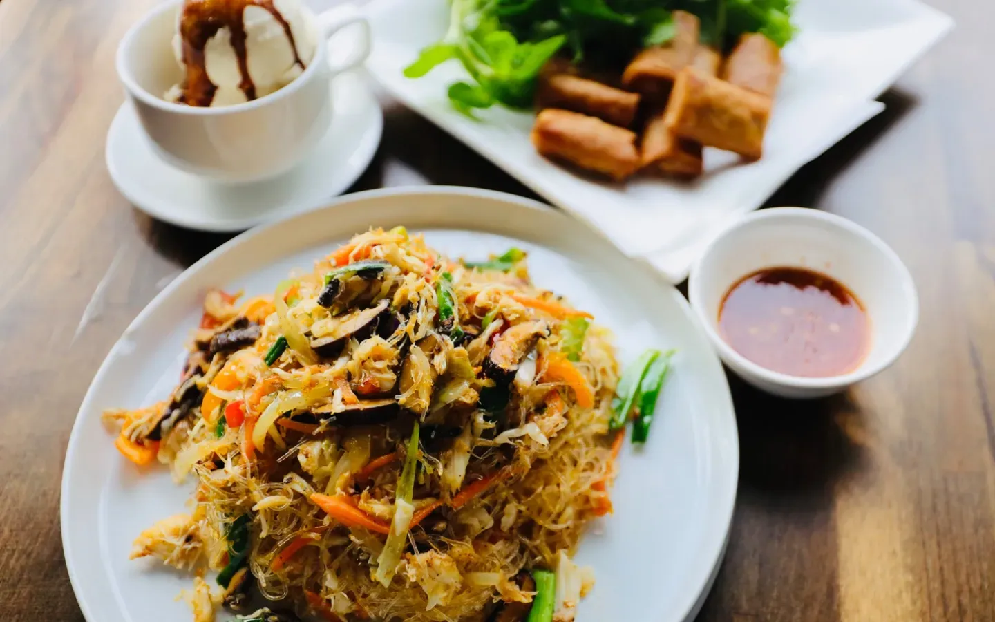 Stir-fried noodles, spring rolls, dipping sauce, and ice cream.