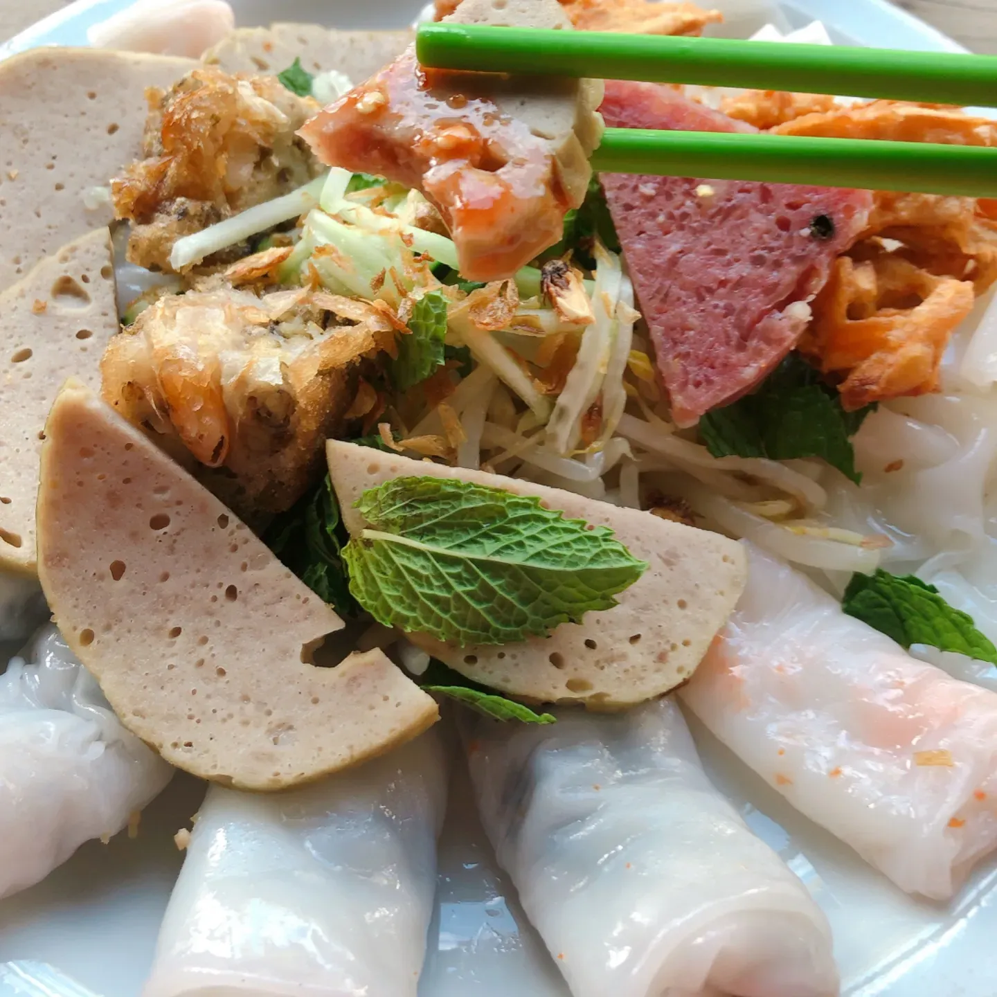 Vietnamese Banh Cuon with sliced meats, fried pieces, and fresh mint.