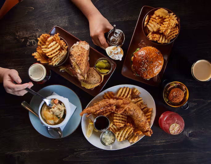 Table with fish and chips, burger, sandwich, pot pie, and drinks.