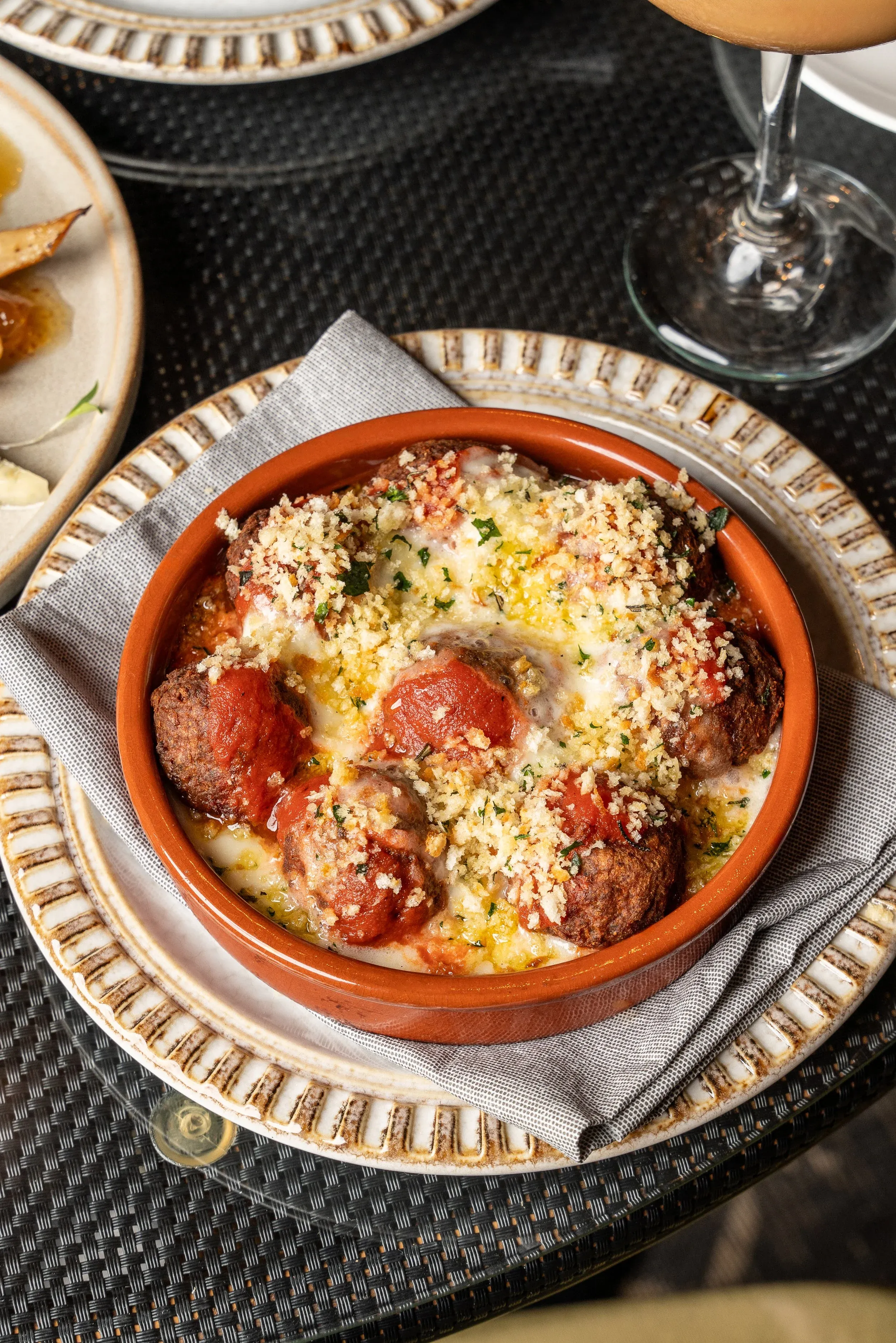 Terracotta bowl of meatballs with tomato sauce, cheese, and breadcrumbs.
