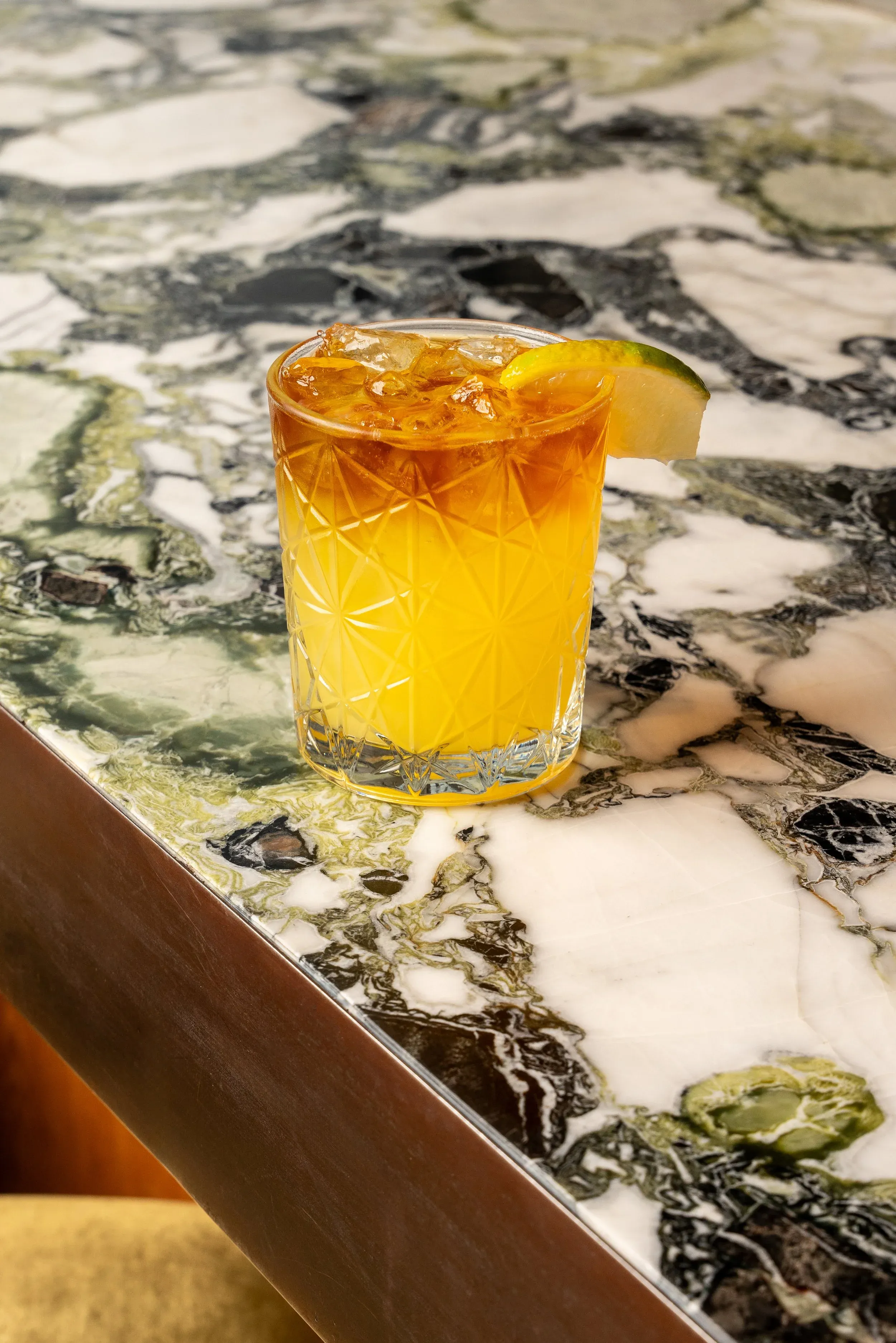 Yellow and brown cocktail with lime on a marble table.