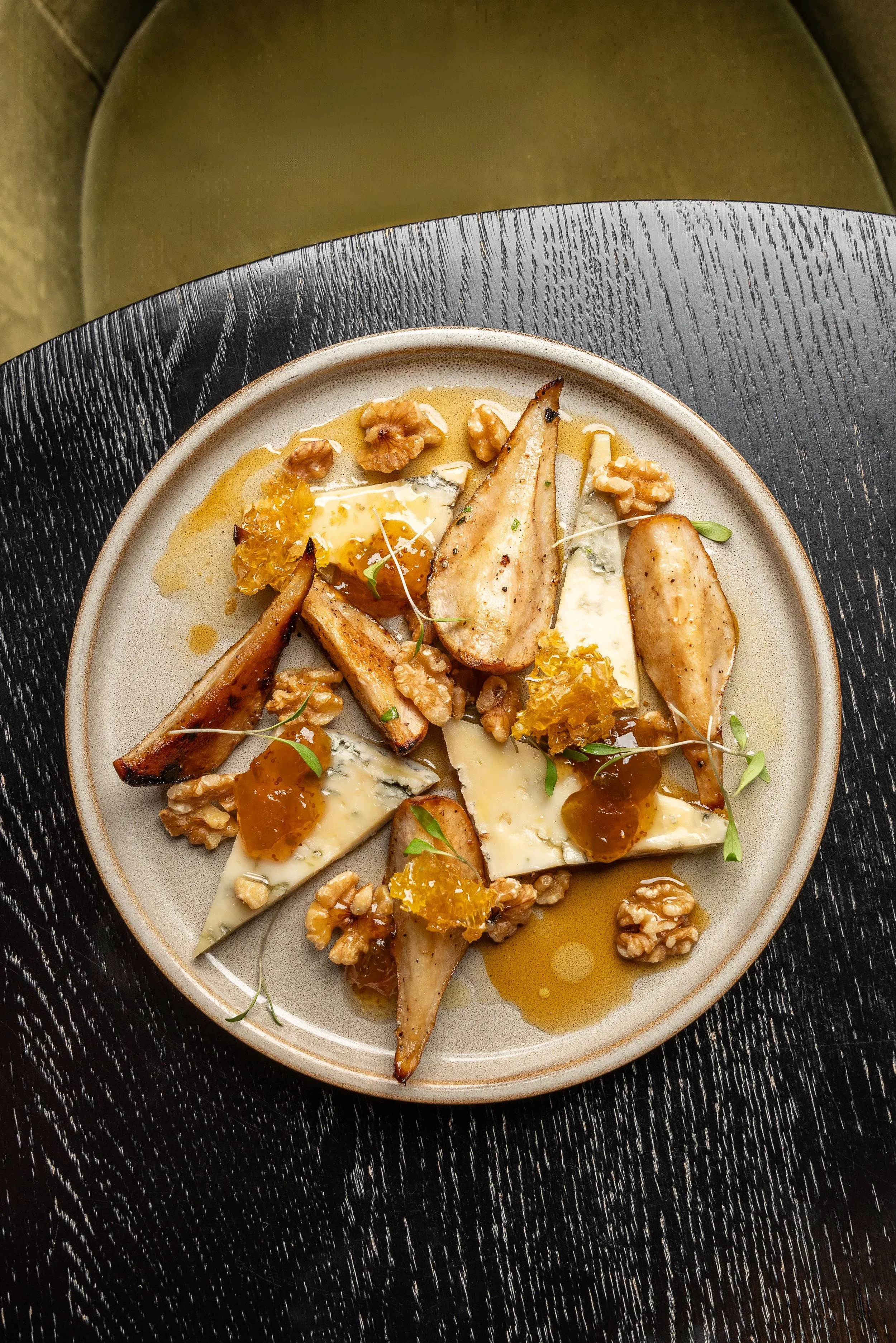 Plate of blue cheese, seared pears, walnuts, and honeycomb on dark table.