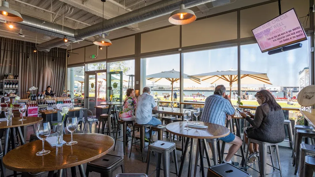 Spacious wine bar with patrons and large windows overlooking water.