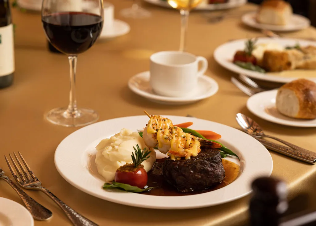 Plate with steak, shrimp skewer, mashed potatoes, and red wine.