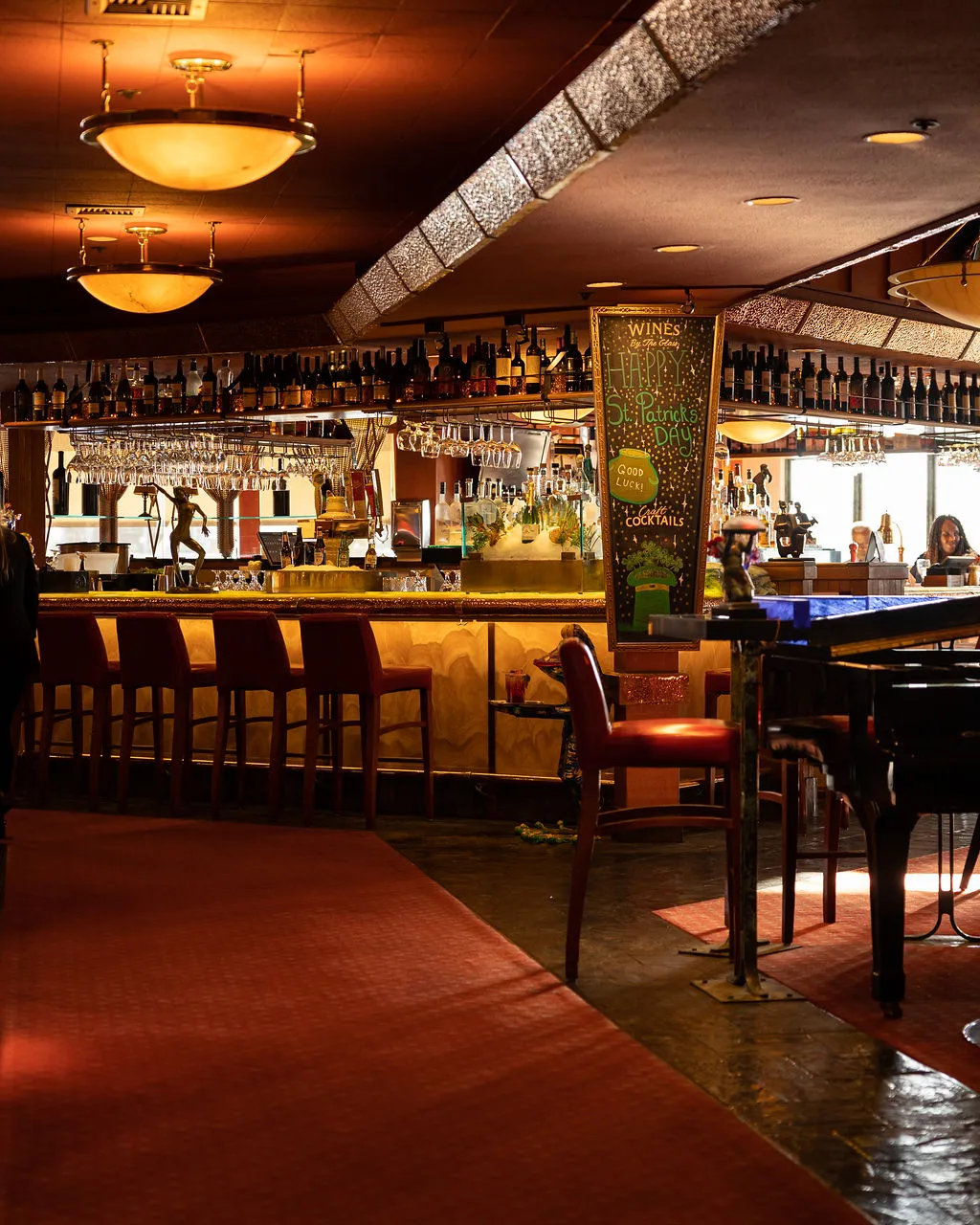 A bar interior with bottles, piano, and a St. Patrick's Day sign.