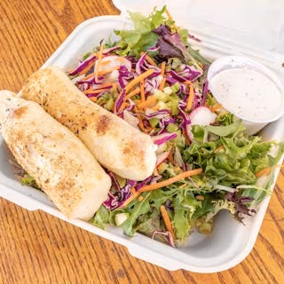 Takeout container with mixed salad, two breadsticks, and a cup of dressing.