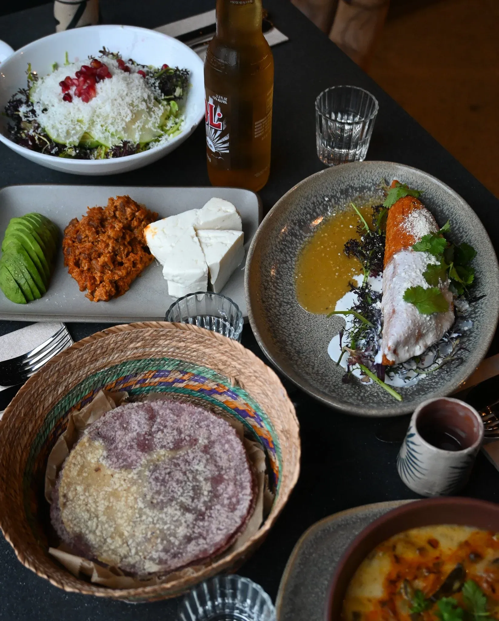 A table full of various Mexican dishes, including salad, tortillas, and beer.