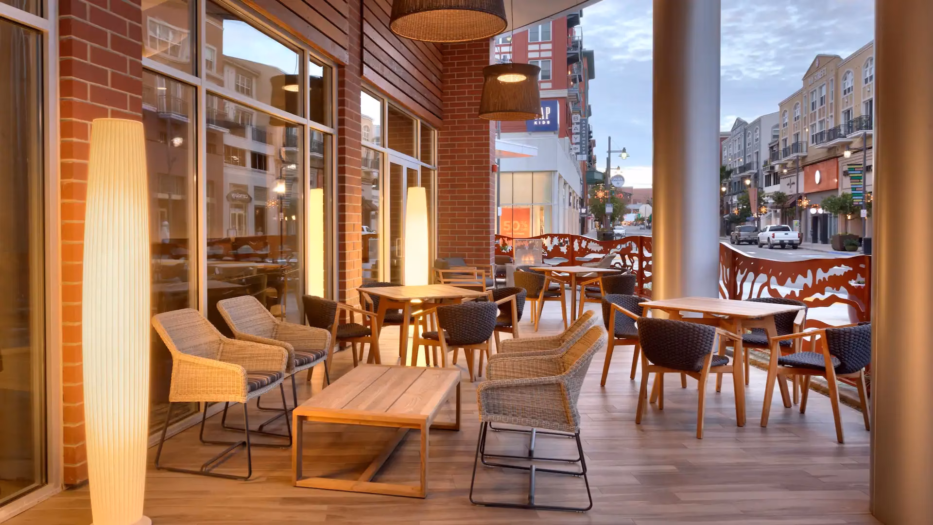 Outdoor patio with tables, chairs, illuminated lamps, and a street view.