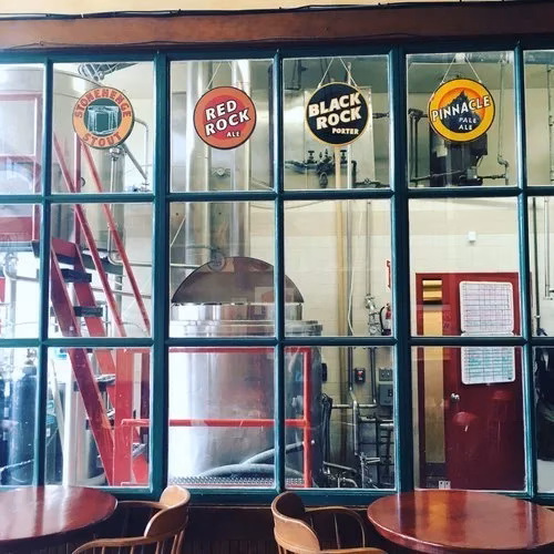 Brewery interior with tanks and beer signs, viewed from seating area.