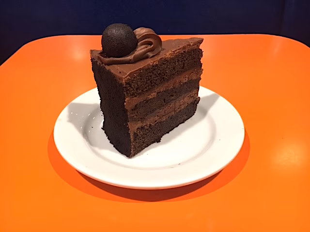 A slice of chocolate layer cake with a chocolate truffle on top.