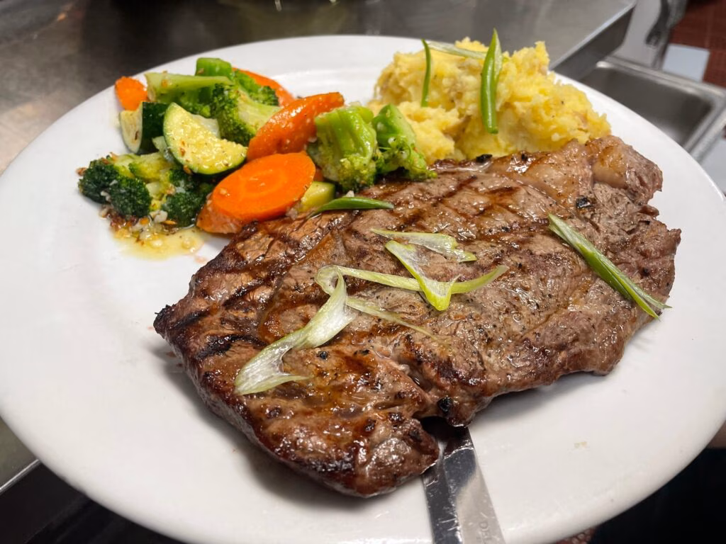 Grilled steak, mashed potatoes, and mixed vegetables on a white plate.