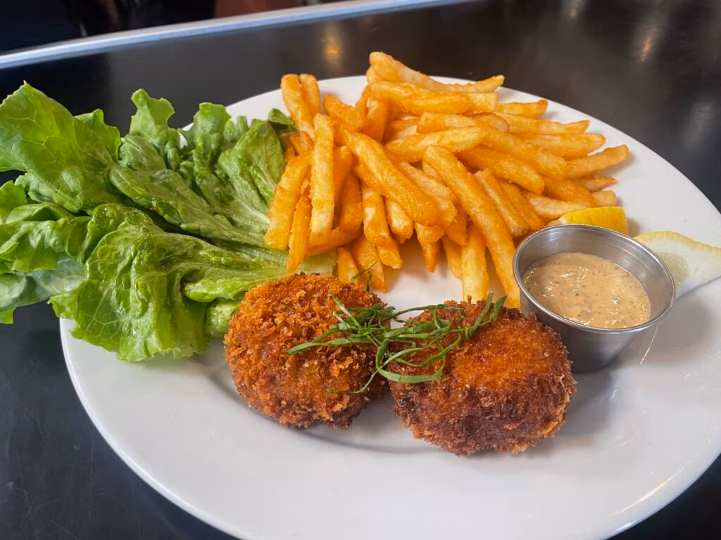 Plate with two fried cakes, french fries, lettuce, sauce, and lemon.