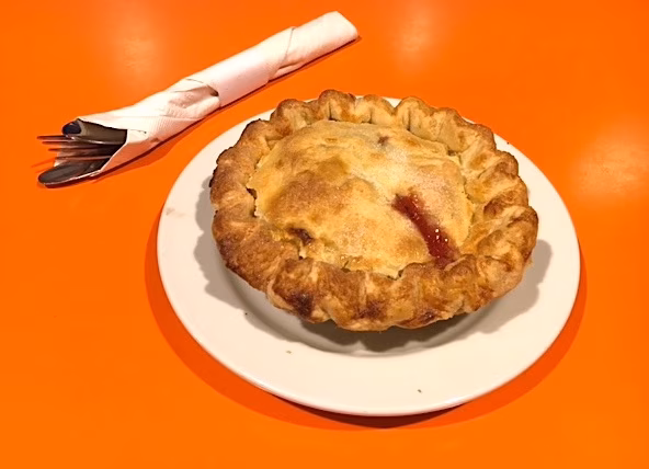 Baked fruit pie on a white plate with wrapped cutlery.