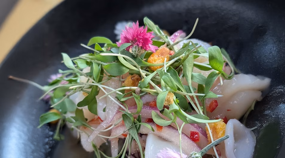 White slices with microgreens, red slivers, golden crumbs, and pink flower.