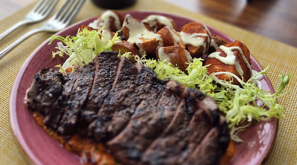 Grilled sliced steak, roasted potatoes, and frisee lettuce on a plate.
